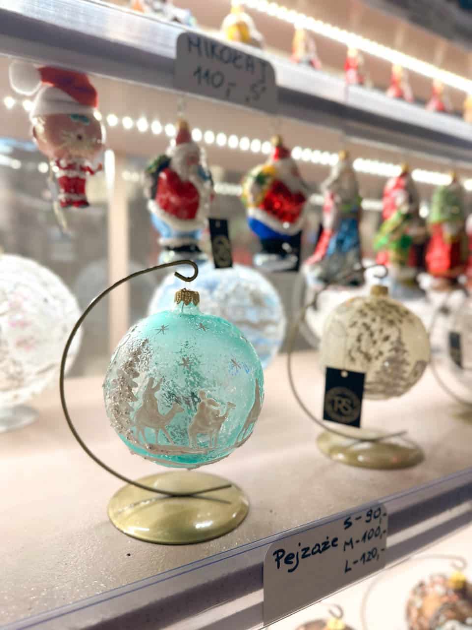 A turquoise glass bauble with a snowy camel scene, displayed alongside other hand-painted Christmas ornaments at the Krak&oacute;w Christmas market