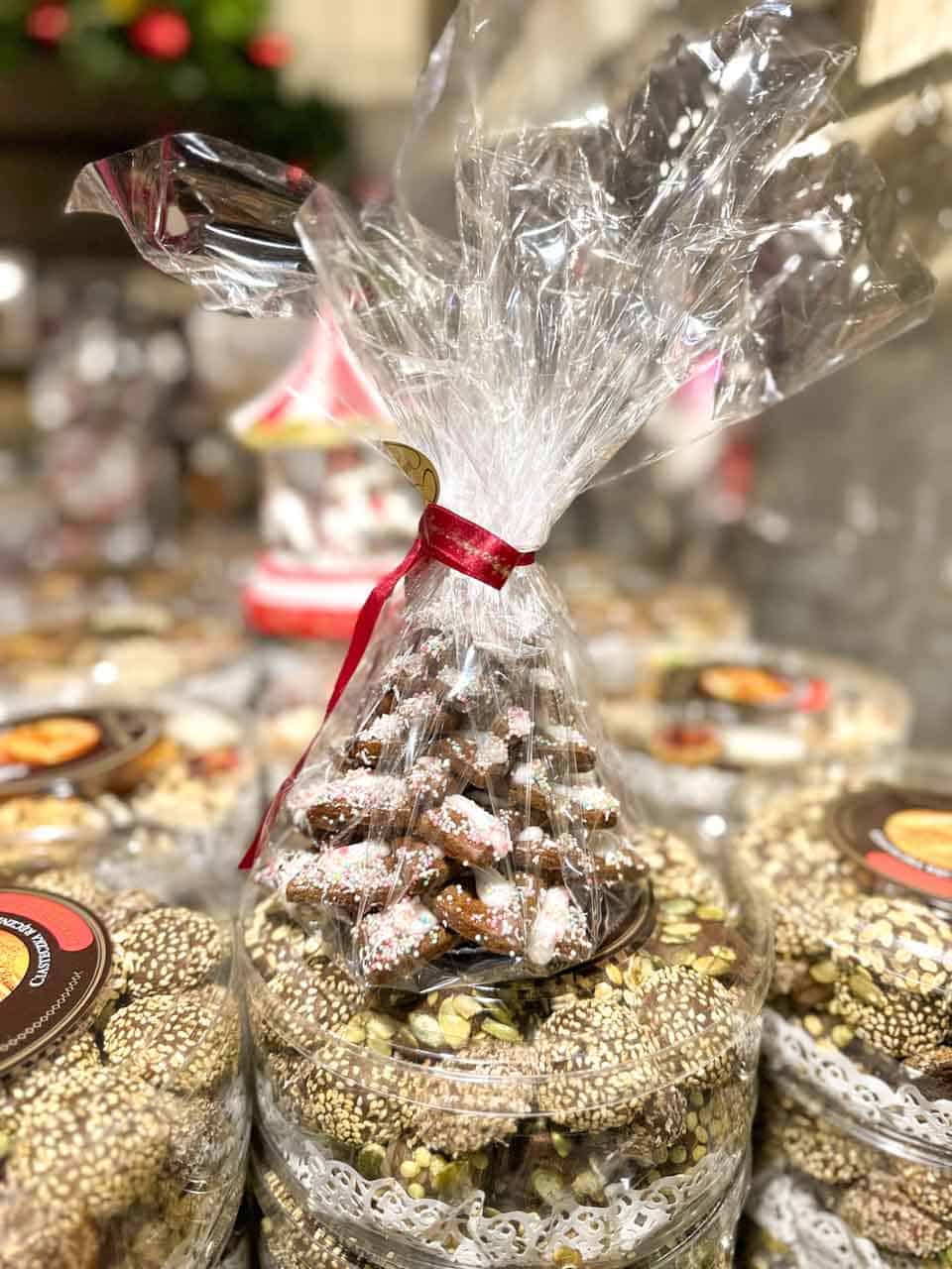 A festive cone-shaped bag of iced gingerbread cookies wrapped in cellophane, surrounded by nut and sesame snacks