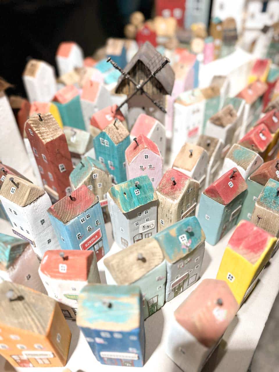 Handmade wooden houses painted in pastel colours, with small signs like 'KINO' and 'SZKOŁA' visible on the fronts