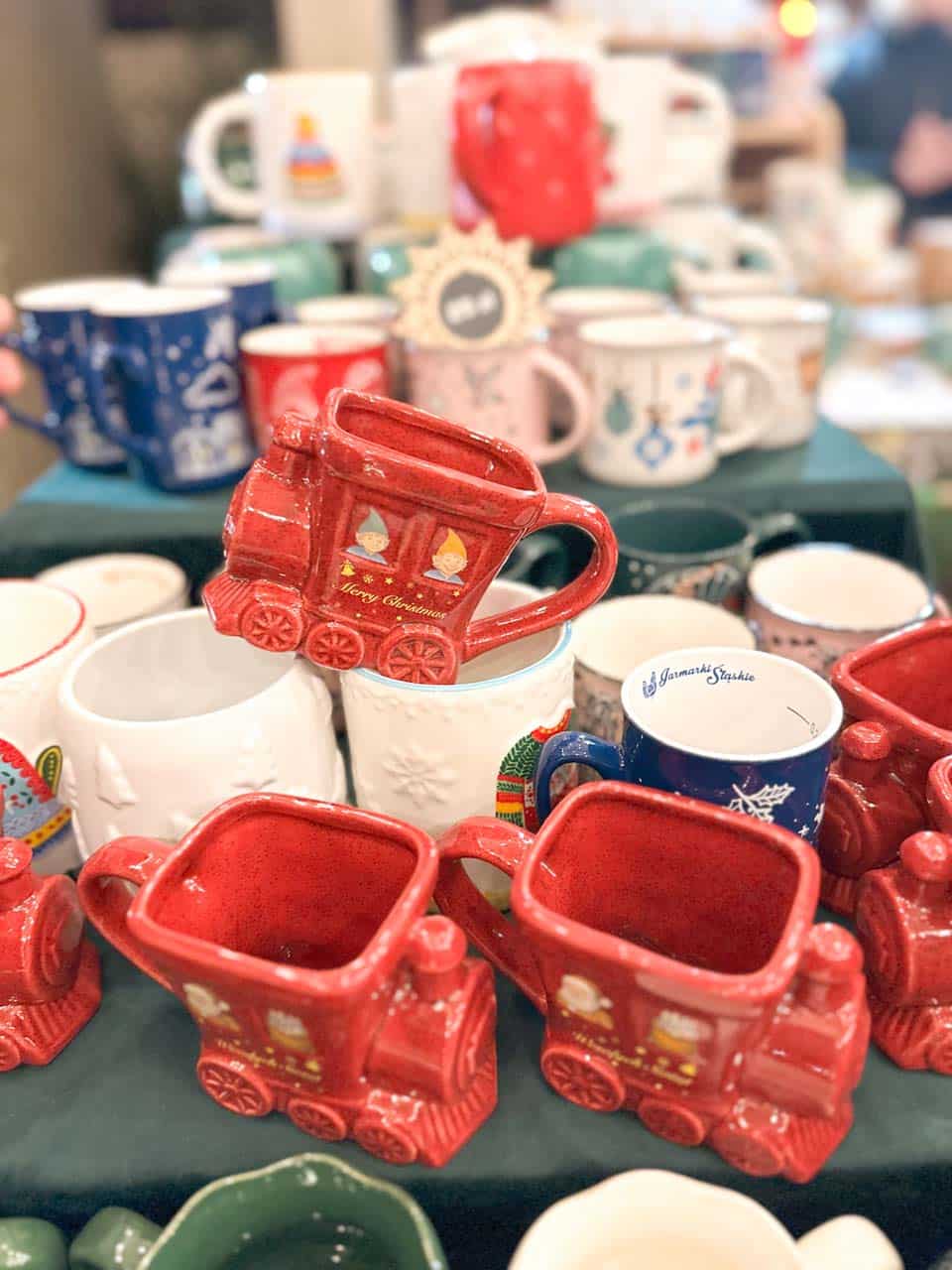 Red ceramic mugs shaped like Christmas trains with &lsquo;Merry Christmas&rsquo; written on the side, displayed with other festive mugs at the Krak&oacute;w Christmas market