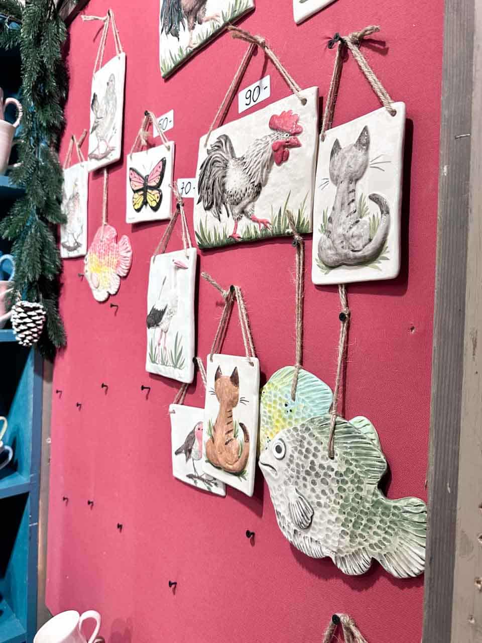 Handmade ceramic wall hangings with animals, fish, and butterflies displayed against a red wall at a Christmas stall in Krak&oacute;w, Poland