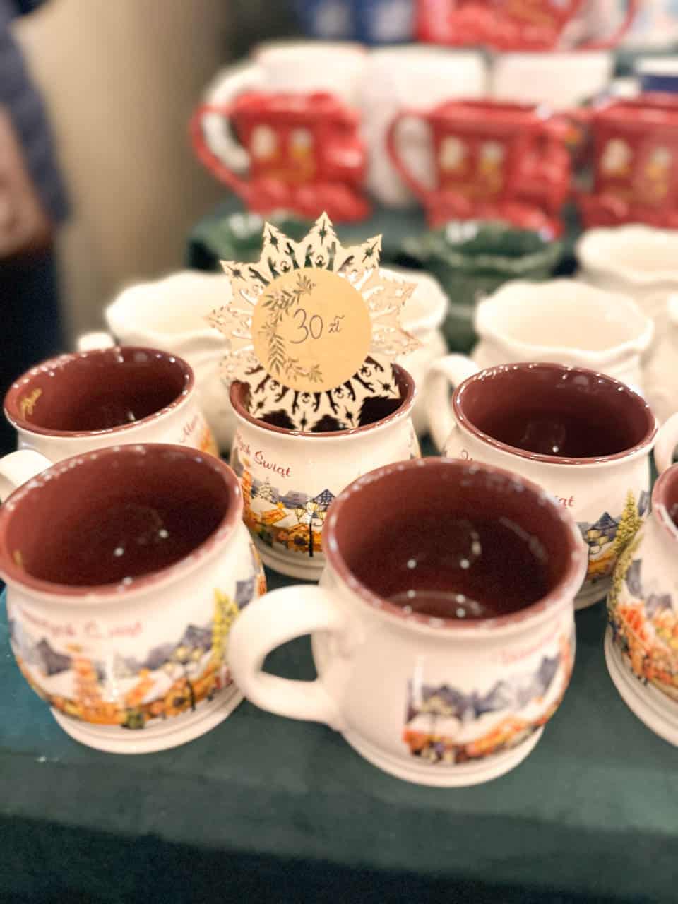 Traditional Polish Christmas mugs with festive village designs, priced at 30 zł, displayed on a market stall in Krak&oacute;w, Poland