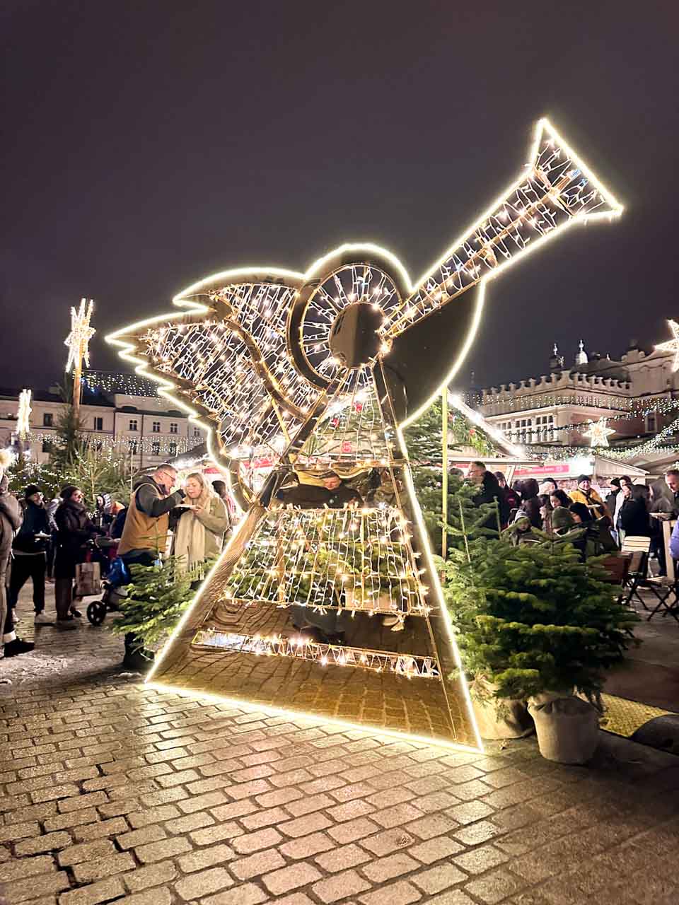 A large glowing Christmas decoration of an angel playing a trumpet, lit up at night in Krak&oacute;w&rsquo;s main square during the Christmas market