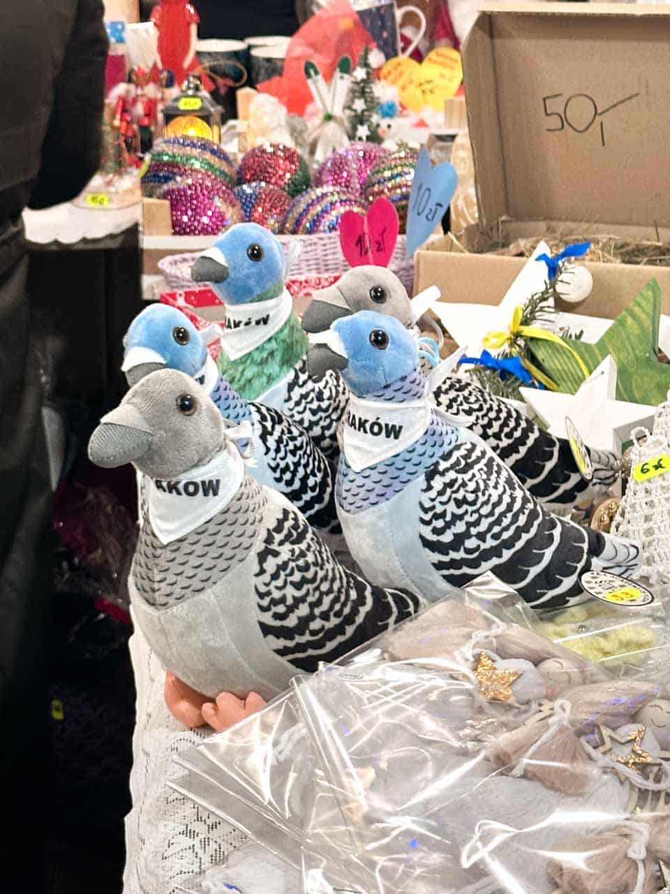 Plush Krak&oacute;w pigeons wearing white scarves on a Christmas market stall surrounded by decorations and ornaments