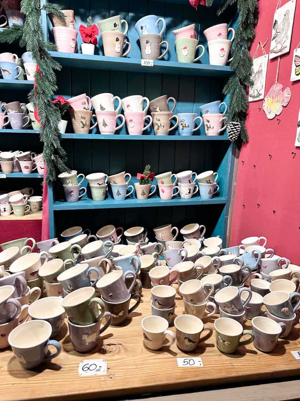 A display of pastel ceramic mugs with festive designs, arranged on blue wooden shelves and a table at the Krak&oacute;w Christmas market