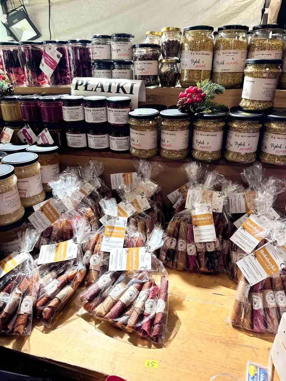 Jars of dried petals, bee pollen, and creamed honey, with bags of rolled fruit leather sweets on a wooden market stall