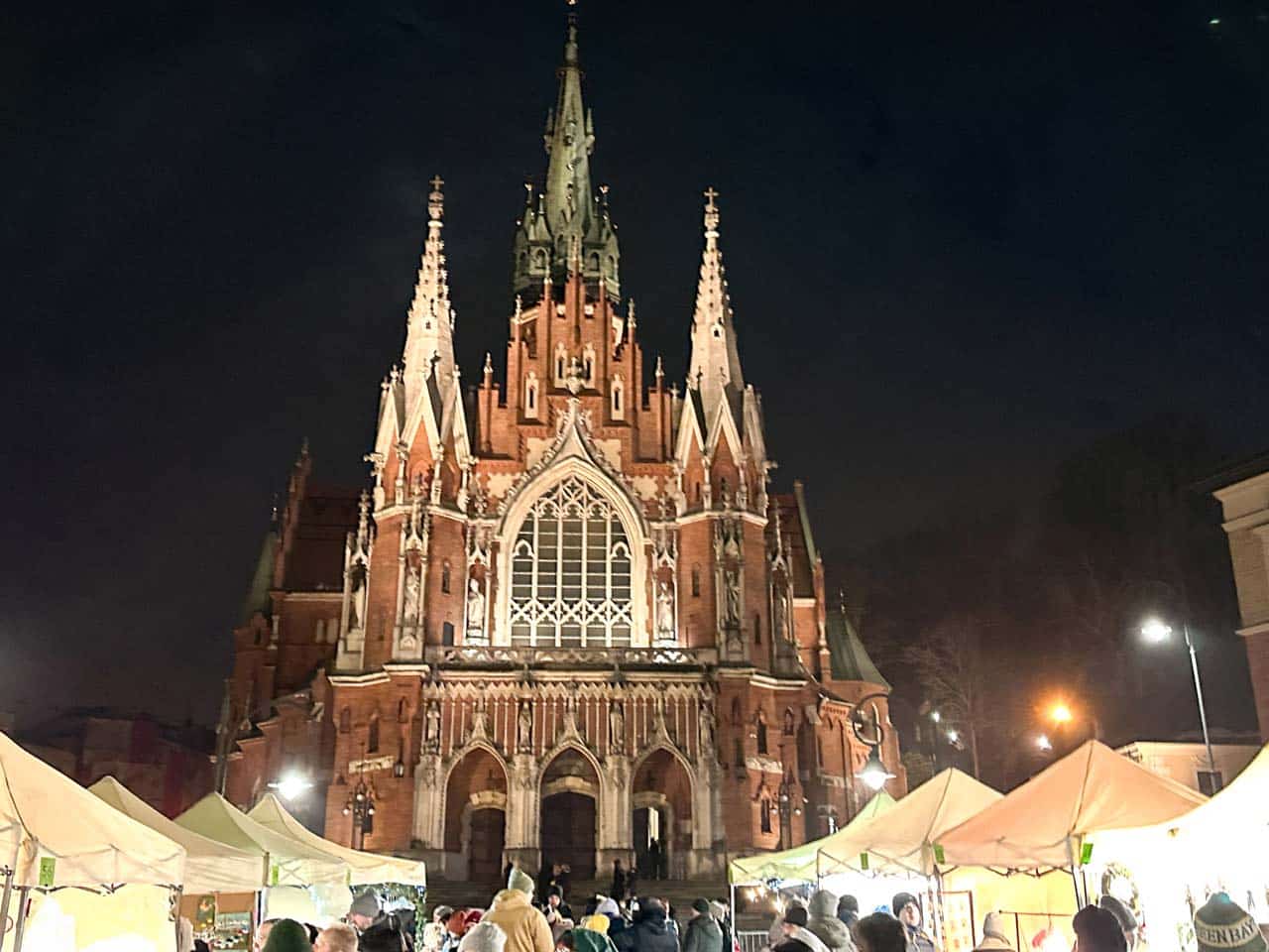 Stalls at the Podg&oacute;rze Christmas market with crowds gathered in front of the illuminated St Joseph&rsquo;s Church at night