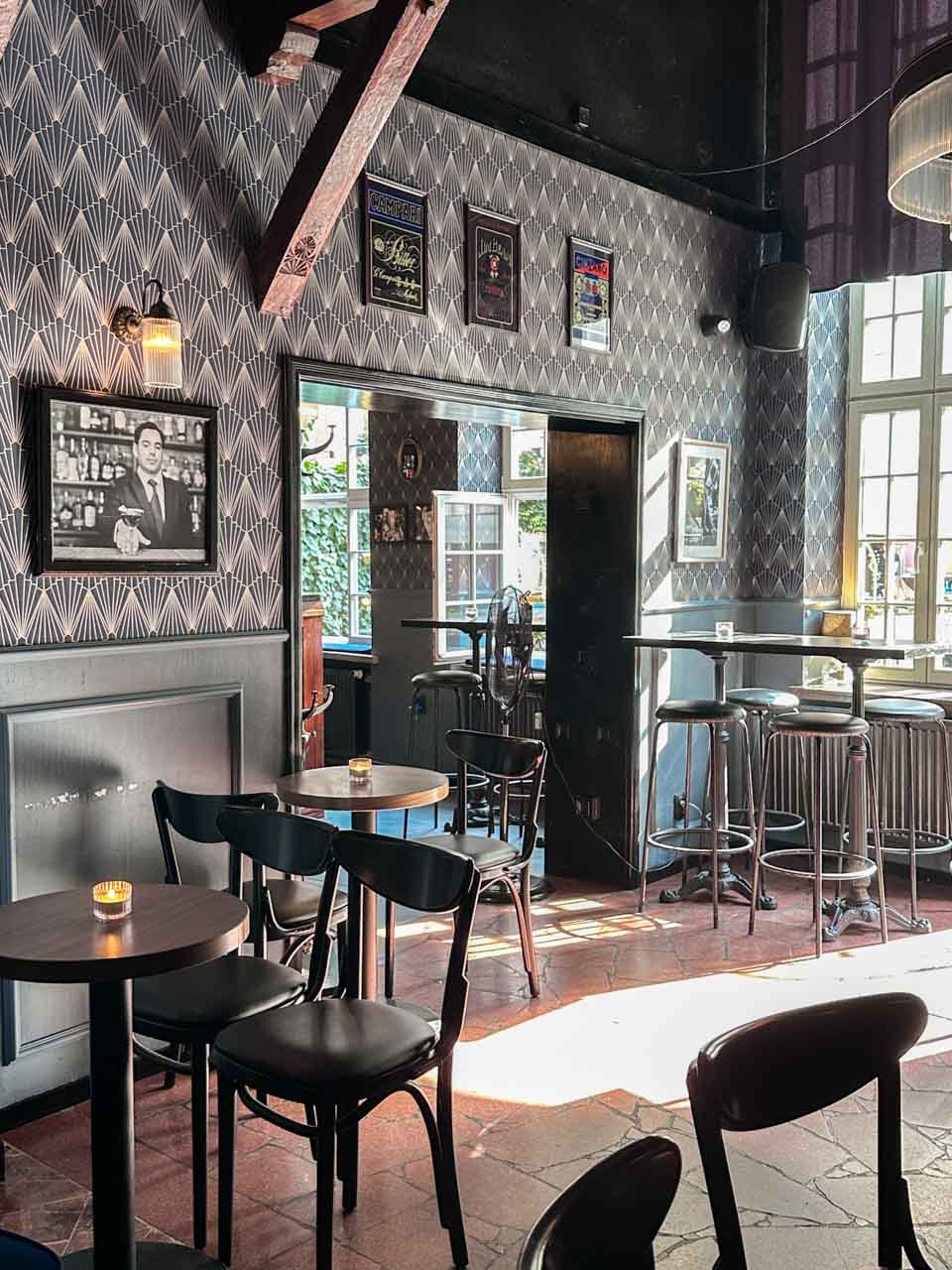 Cosy interior of Craft Cocktails in Gdańsk with patterned wallpaper, framed posters, and round tables lit by tealight candles