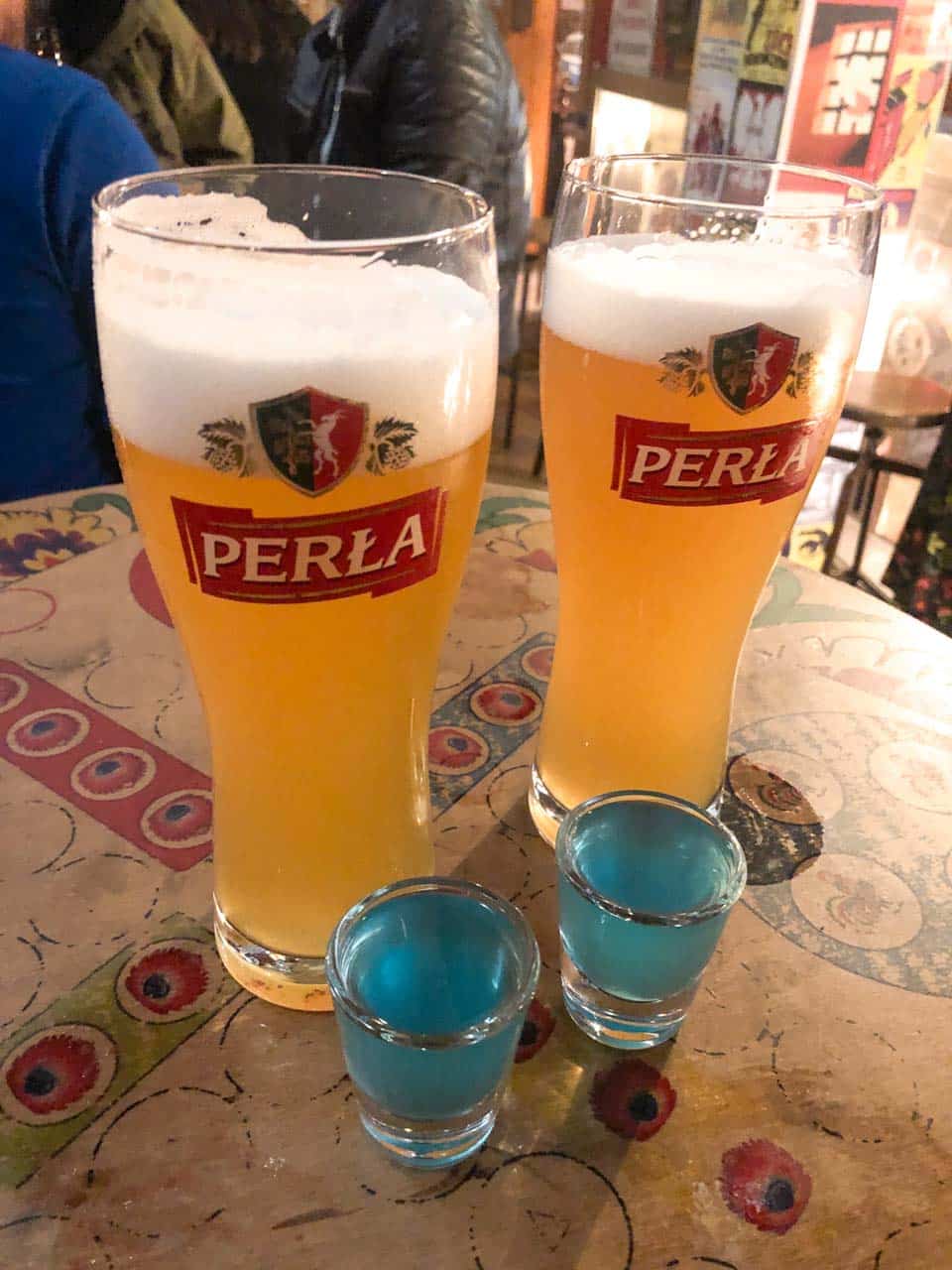 Two Perła beers and two bright blue shots on a painted table at No To Cyk in Gdańsk, Poland