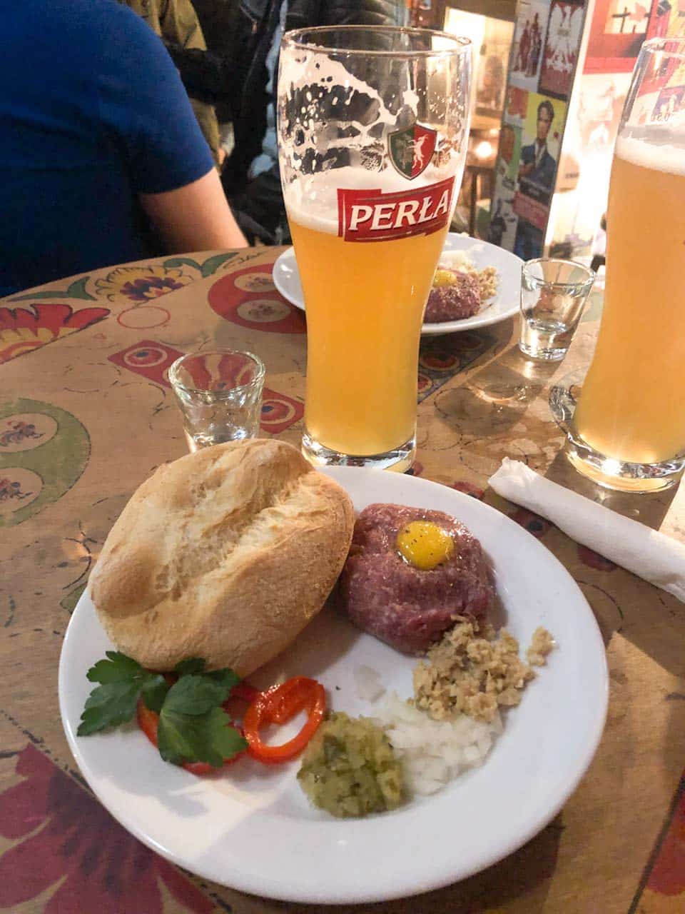 Plate of steak tartare with a bread roll, pickles, onion, and egg yolk, served with Perła beer at No To Cyk in Gdańsk, Poland