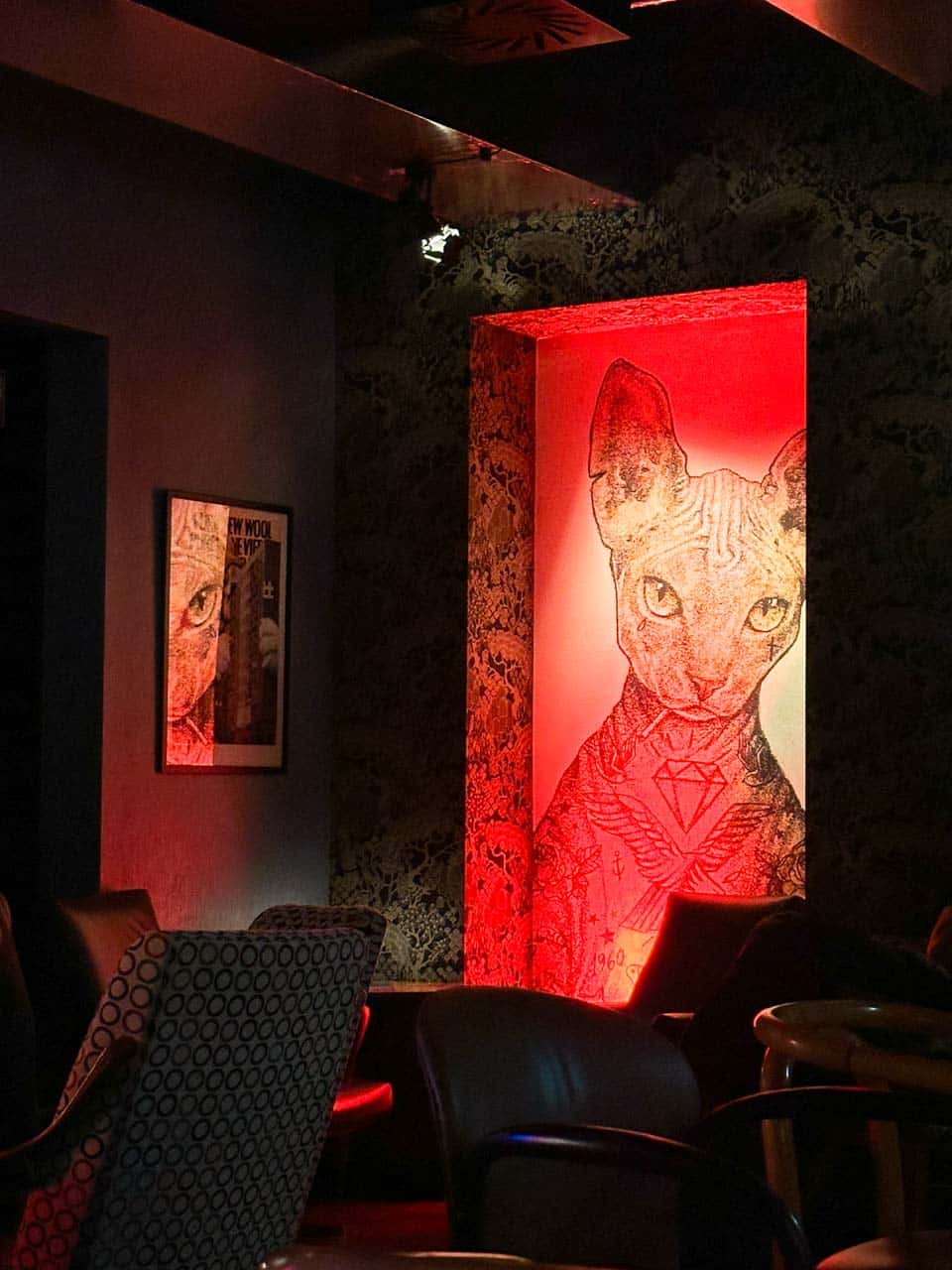 Lounge area of MONK in Gdańsk, Poland, with a glowing red artwork of a tattooed Sphynx cat on the wall and patterned armchairs