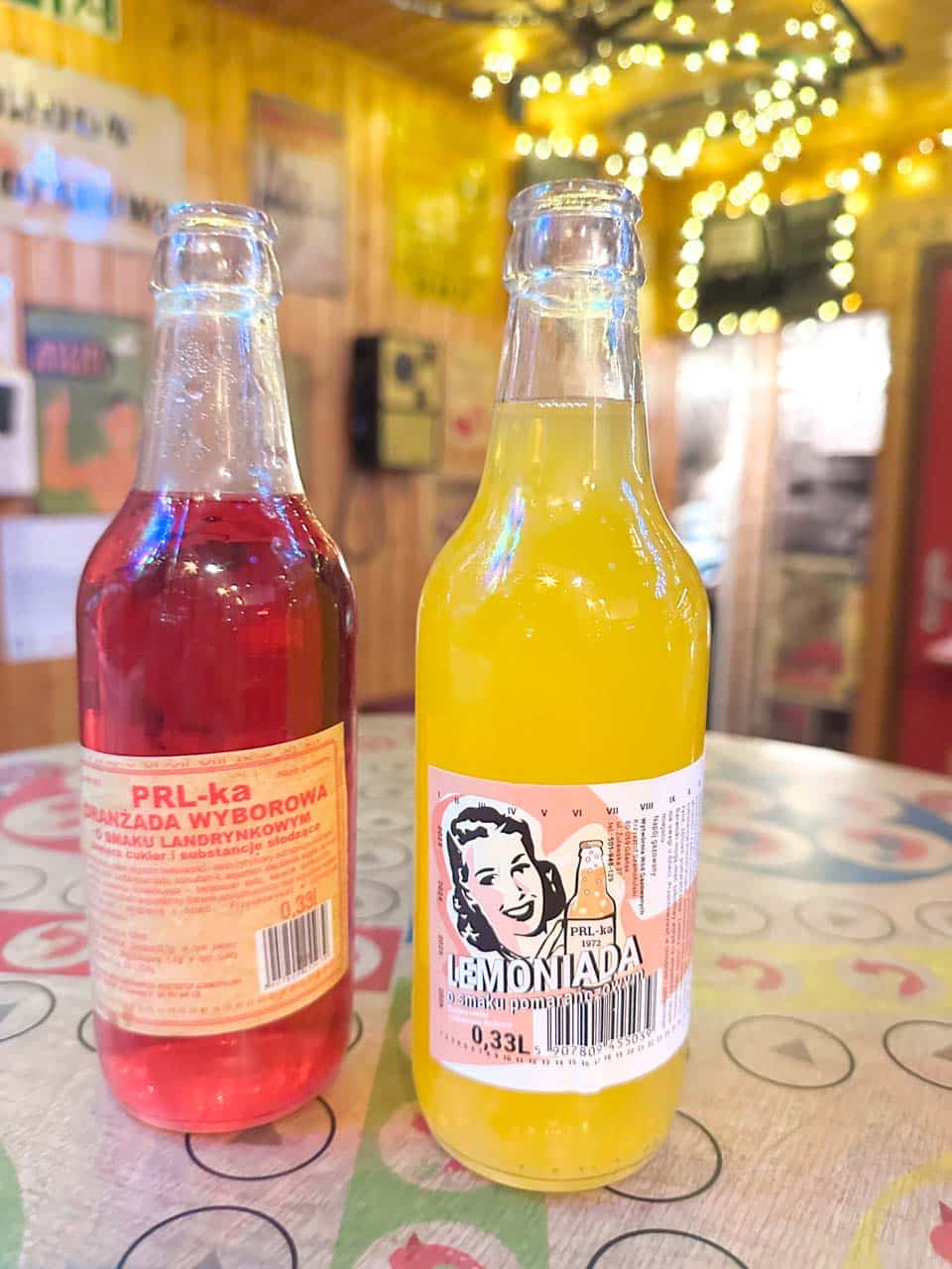 Two retro glass bottles of PRL-style lemonade on a colourful table inside No To Cyk in Gdańsk, Poland
