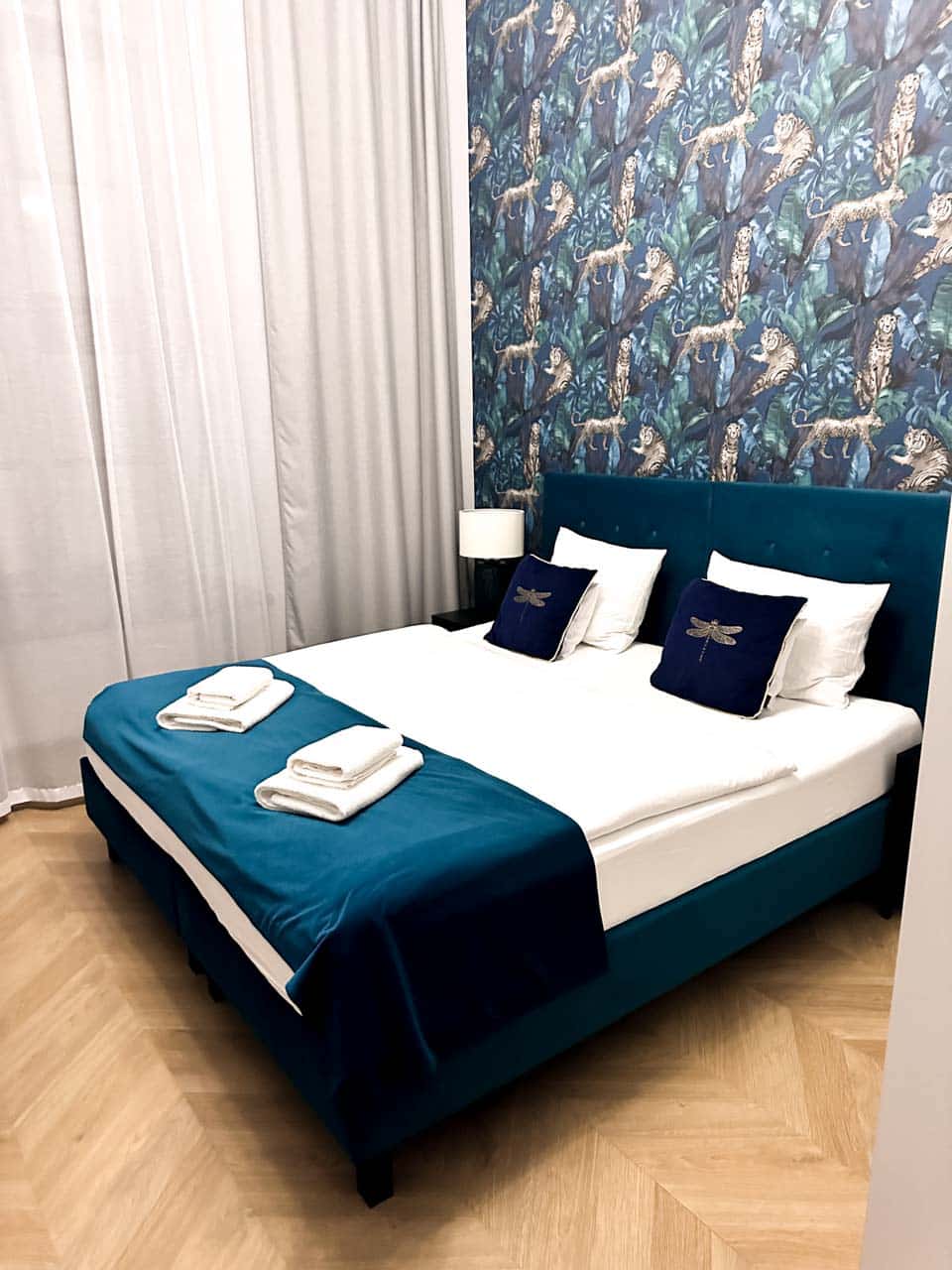 A cosy bedroom with a blue velvet bed, dragonfly cushions, and a bold jungle-print feature wall with leopards