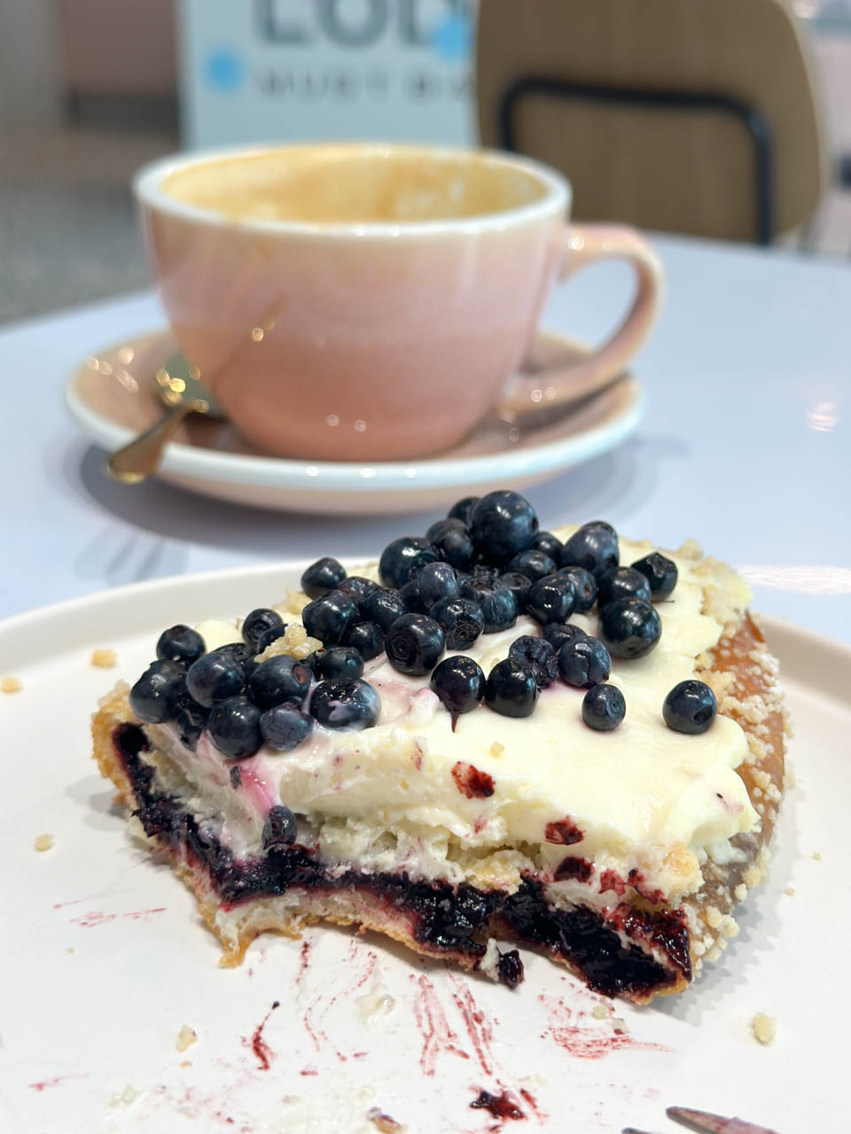Partly eaten bilberry bun with cream and fresh berries served with a pink cup of coffee at Must Bake in Gdańsk, Poland