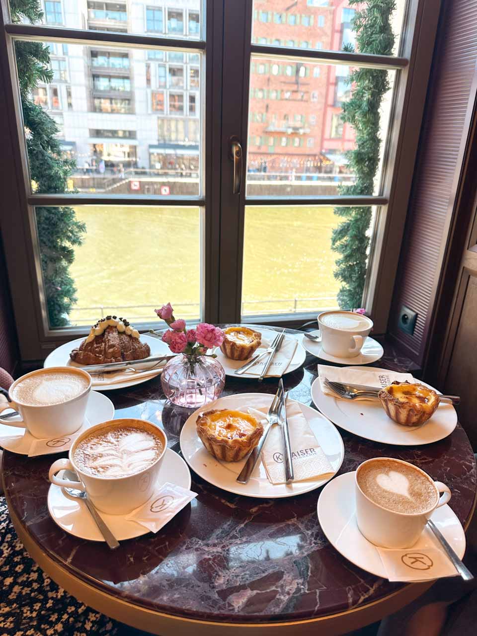 Coffee, three custard tarts, and a cream-filled croissant on a marble table by the window at Kaiser Patisserie, overlooking the Motława River in Gdańsk