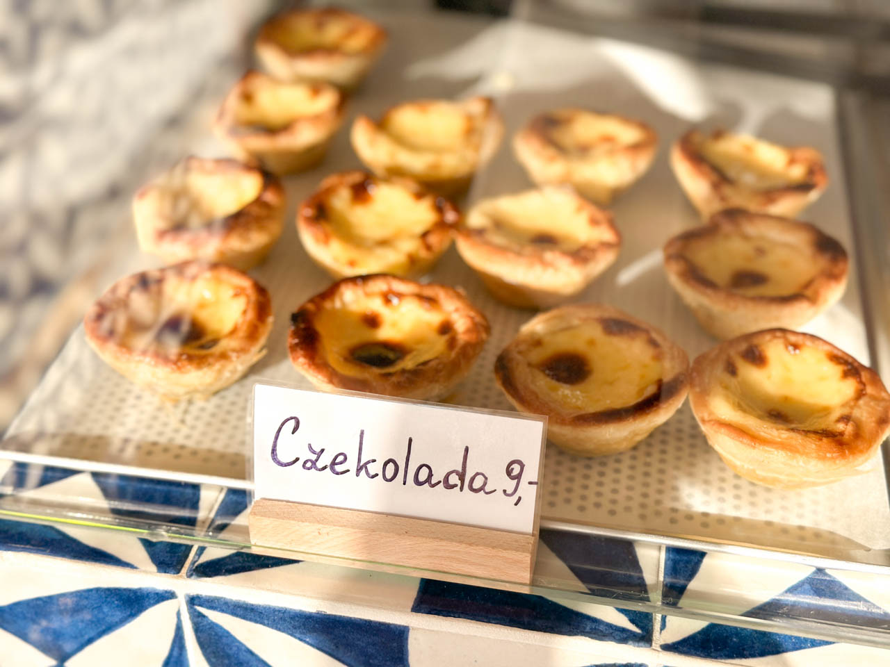 Chocolate custard tarts in a bakery display case with a handwritten price sign