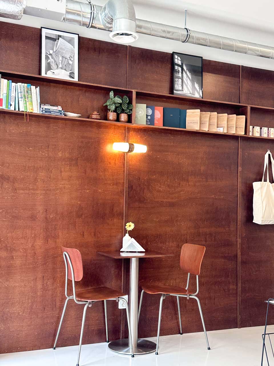 Minimalist caf&eacute; corner with wooden wall panels, small table, chairs, and books on a shelf