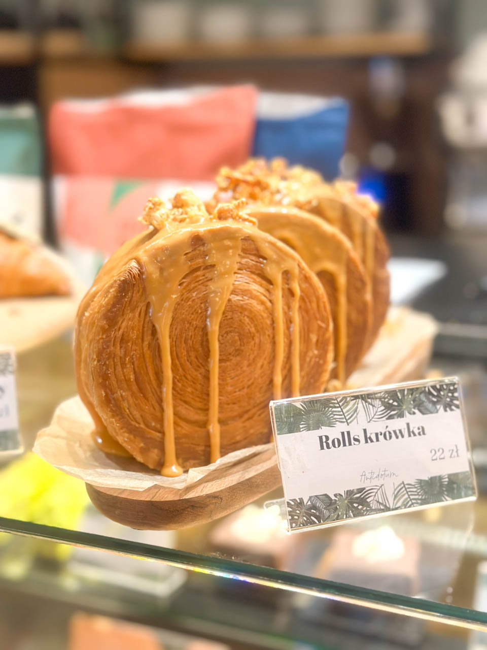 Large caramel-filled New York roll pastries on a wooden tray inside a bakery display at Cafe Antidotum in Gdańsk