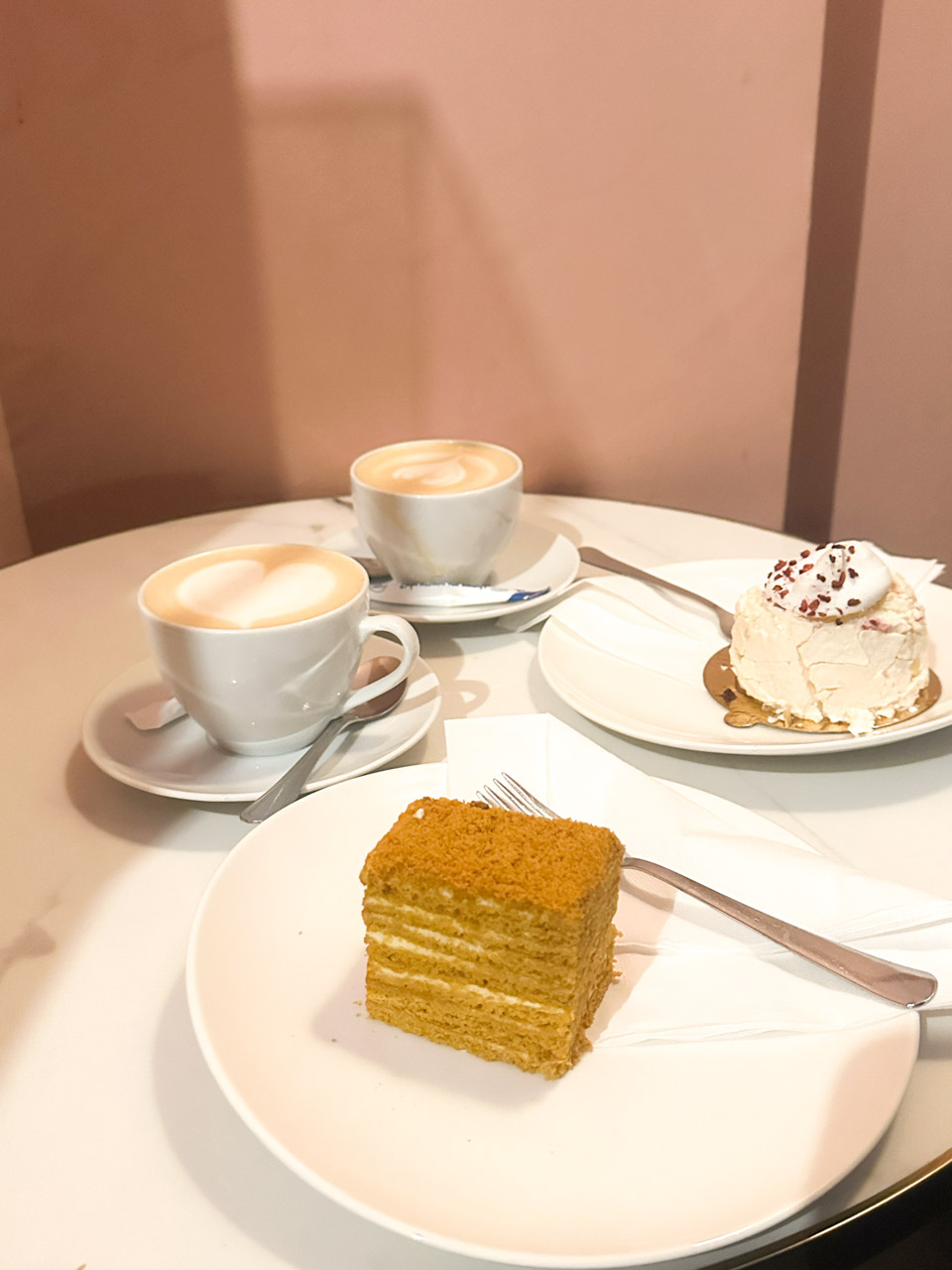 A layered honey cake and a small meringue served with two coffees on a round table at Le Delice in Gdańsk