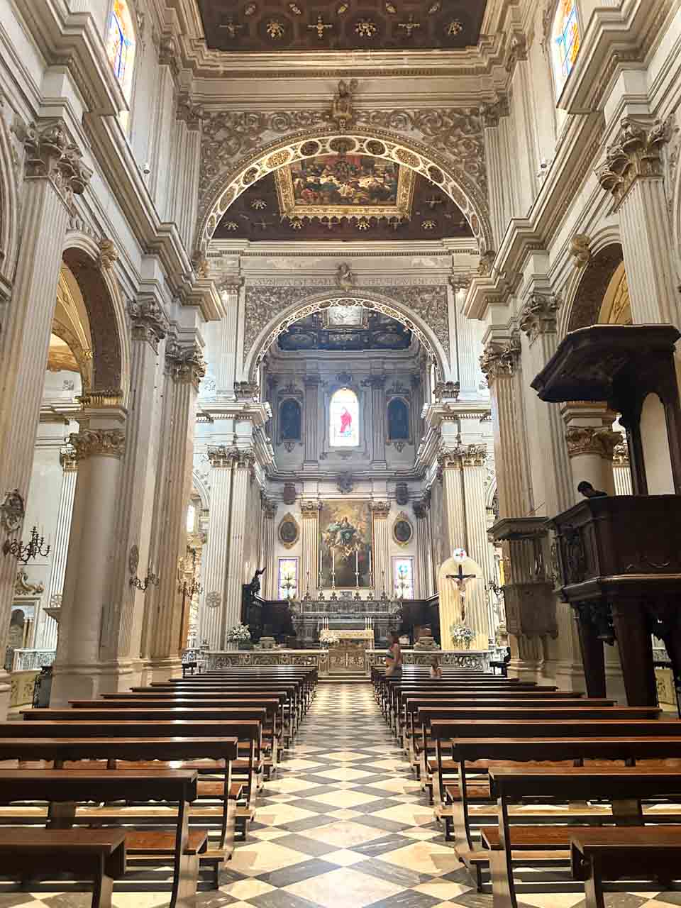 Interior of Lecce Cathedral with tall columns, painted arches, and the main altar