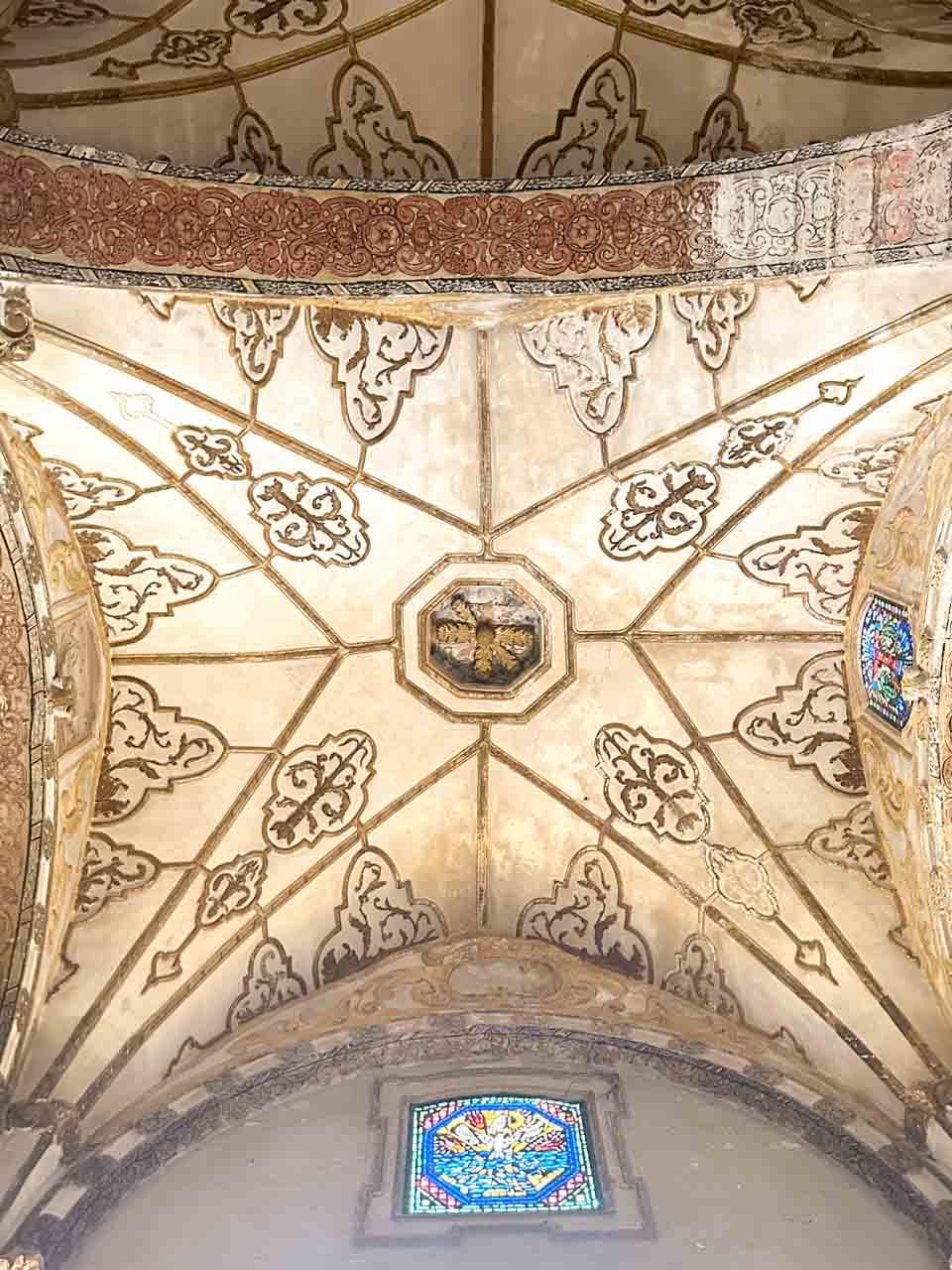 Decorated ceiling vault with painted patterns and a stained glass window inside Lecce Cathedral