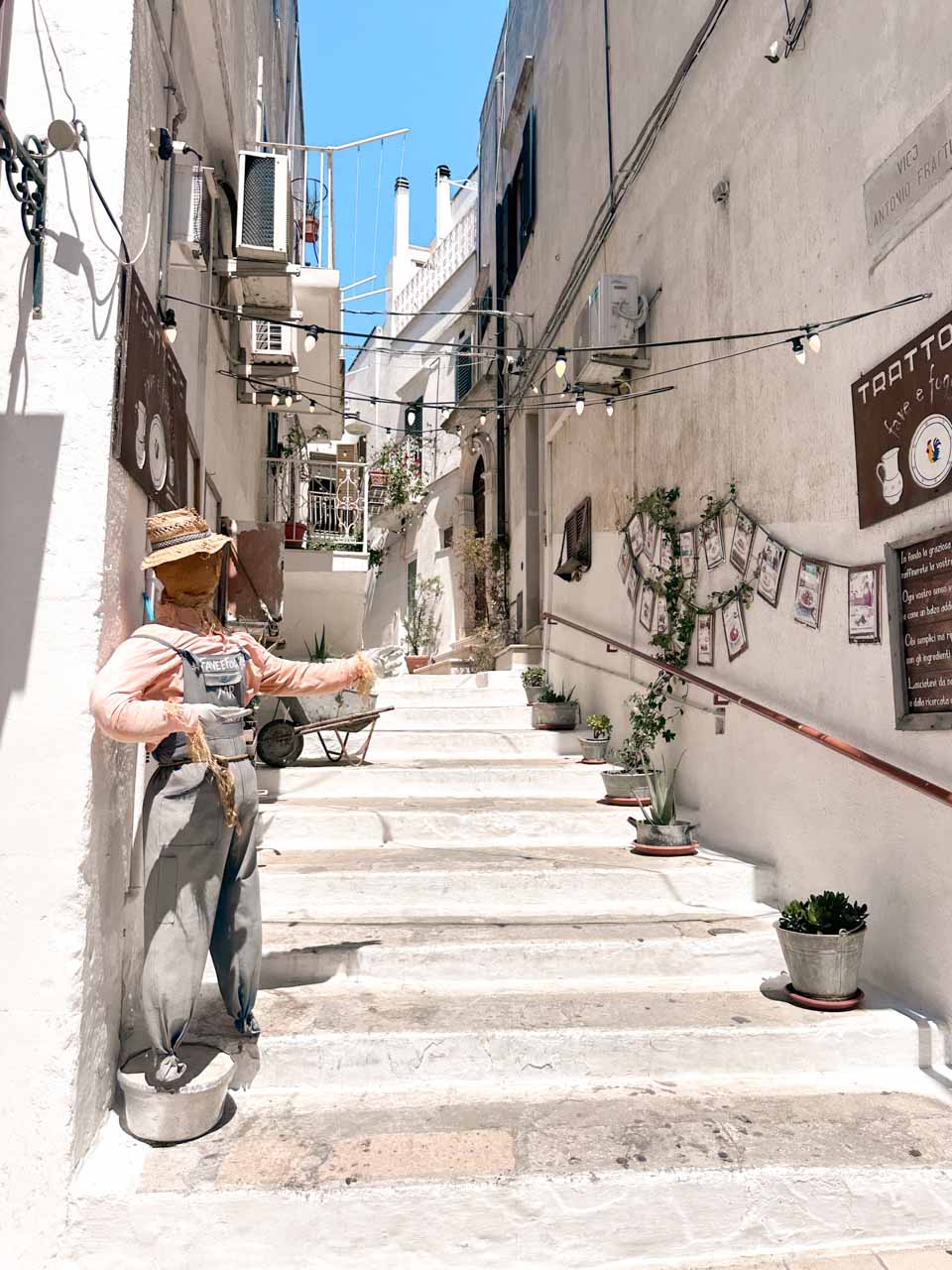 Whitewashed staircase with potted plants and a scarecrow figure in Ostuni&rsquo;s historic centre