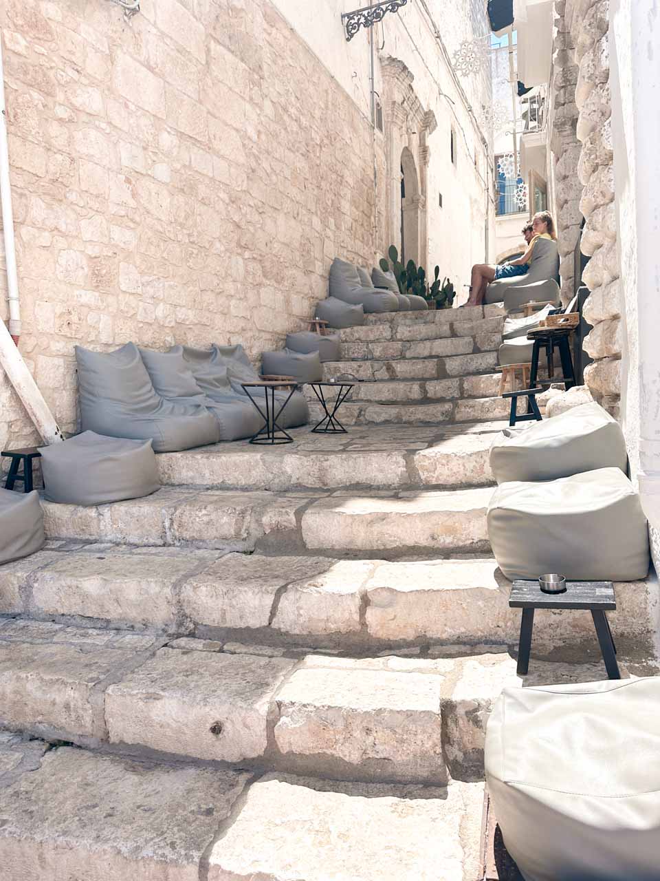 Stone steps with outdoor seating and cushions set up along a narrow street in Ostuni, Italy