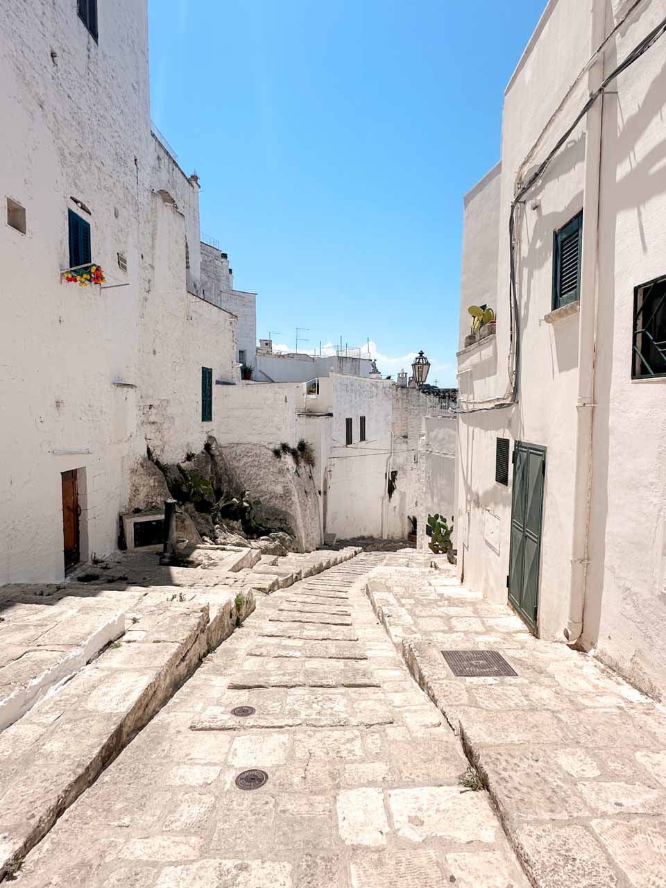 Sloping stone street lined with whitewashed houses and green shutters in Ostuni, Italy
