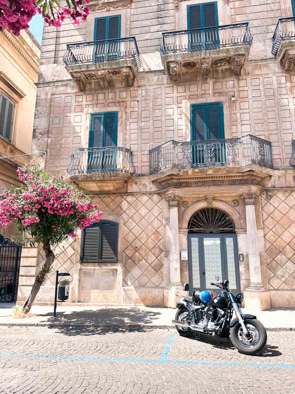 Historic building with balconies and green shutters and a motorbike parked outside in Ostuni, Italy