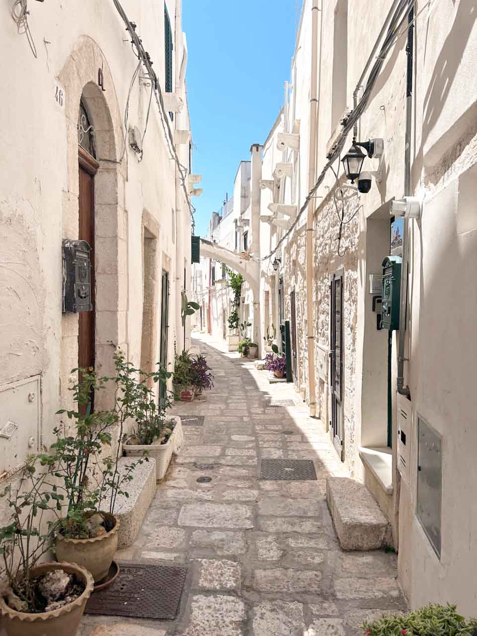 Narrow whitewashed alley with stone paving and potted plants in Ostuni&rsquo;s historic centre