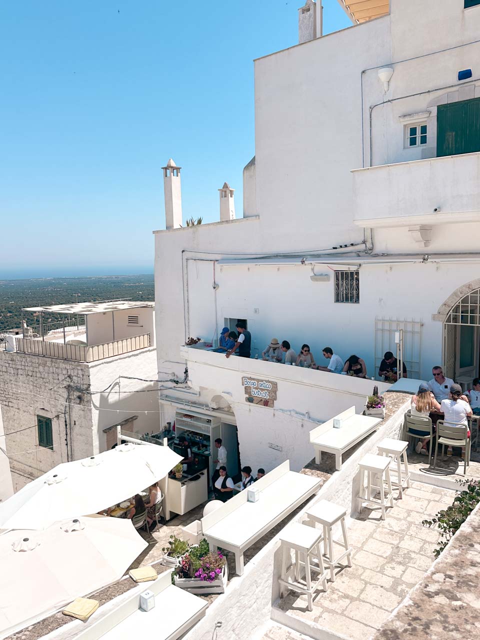 Terrace at Borgo Antico Bistrot with white tables and people dining overlooking Ostuni and the countryside