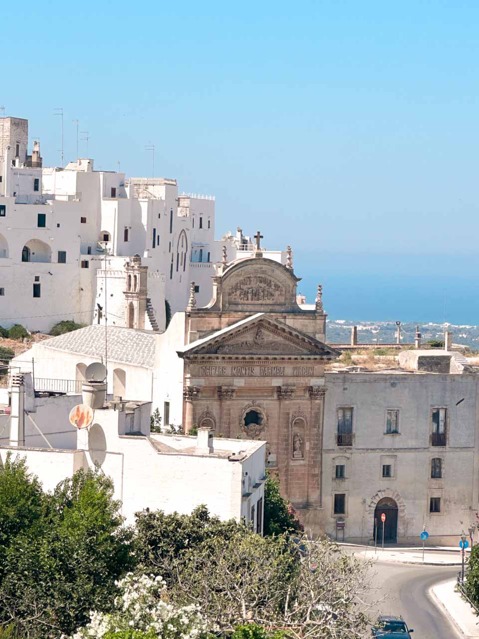 View of Ostuni&rsquo;s whitewashed buildings and a church fa&ccedil;ade with the Adriatic Sea in the distance