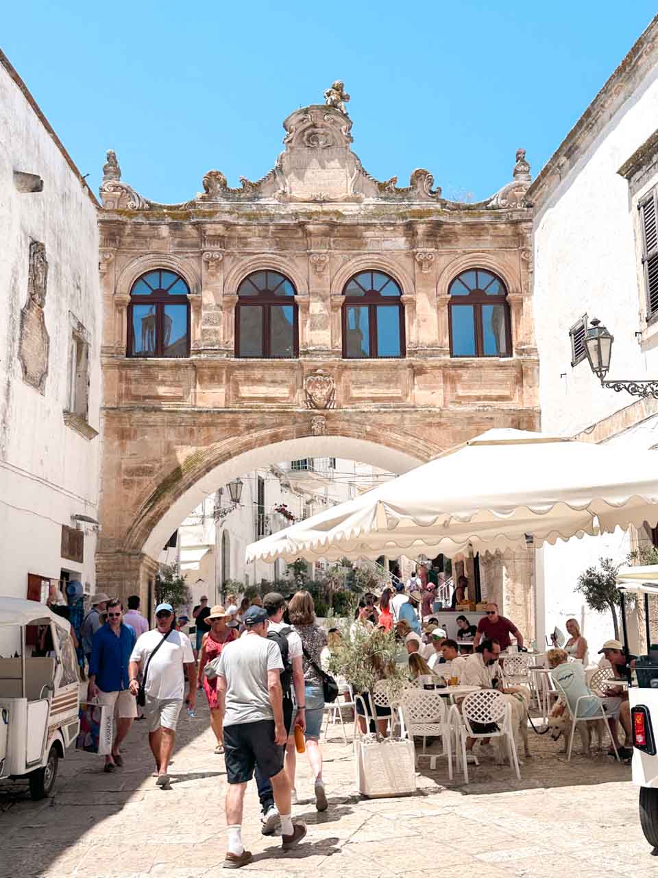 Stone arch bridge (Arco Scoppa) over a busy street with caf&eacute;s and people in Ostuni old town