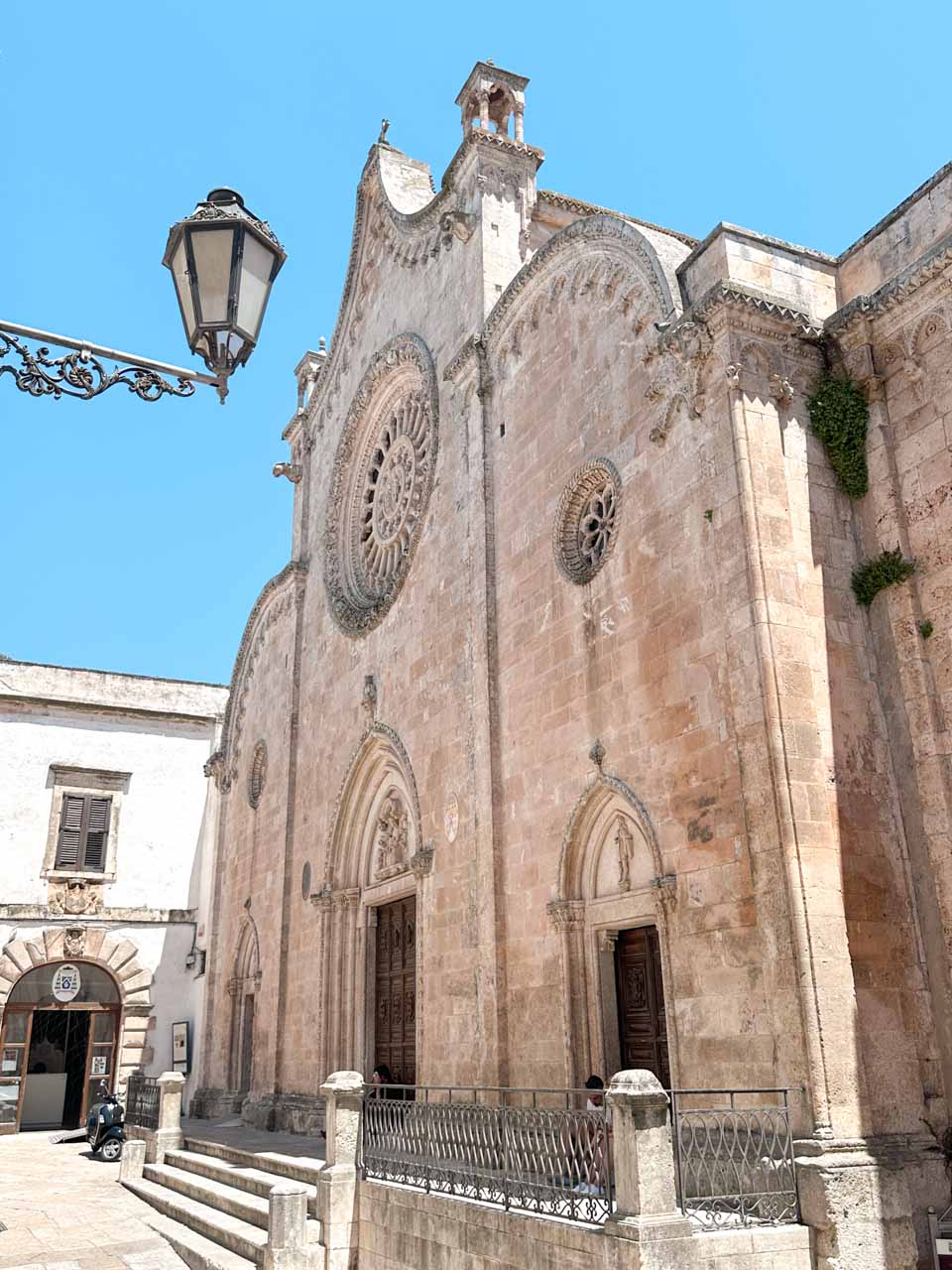 Facade of Ostuni Cathedral with a rose window and stone carvings under a clear blue sky