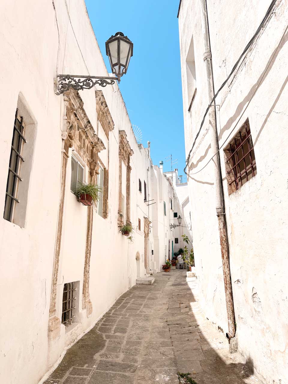 Narrow white alley with stone pavement and balconies in Ostuni old town