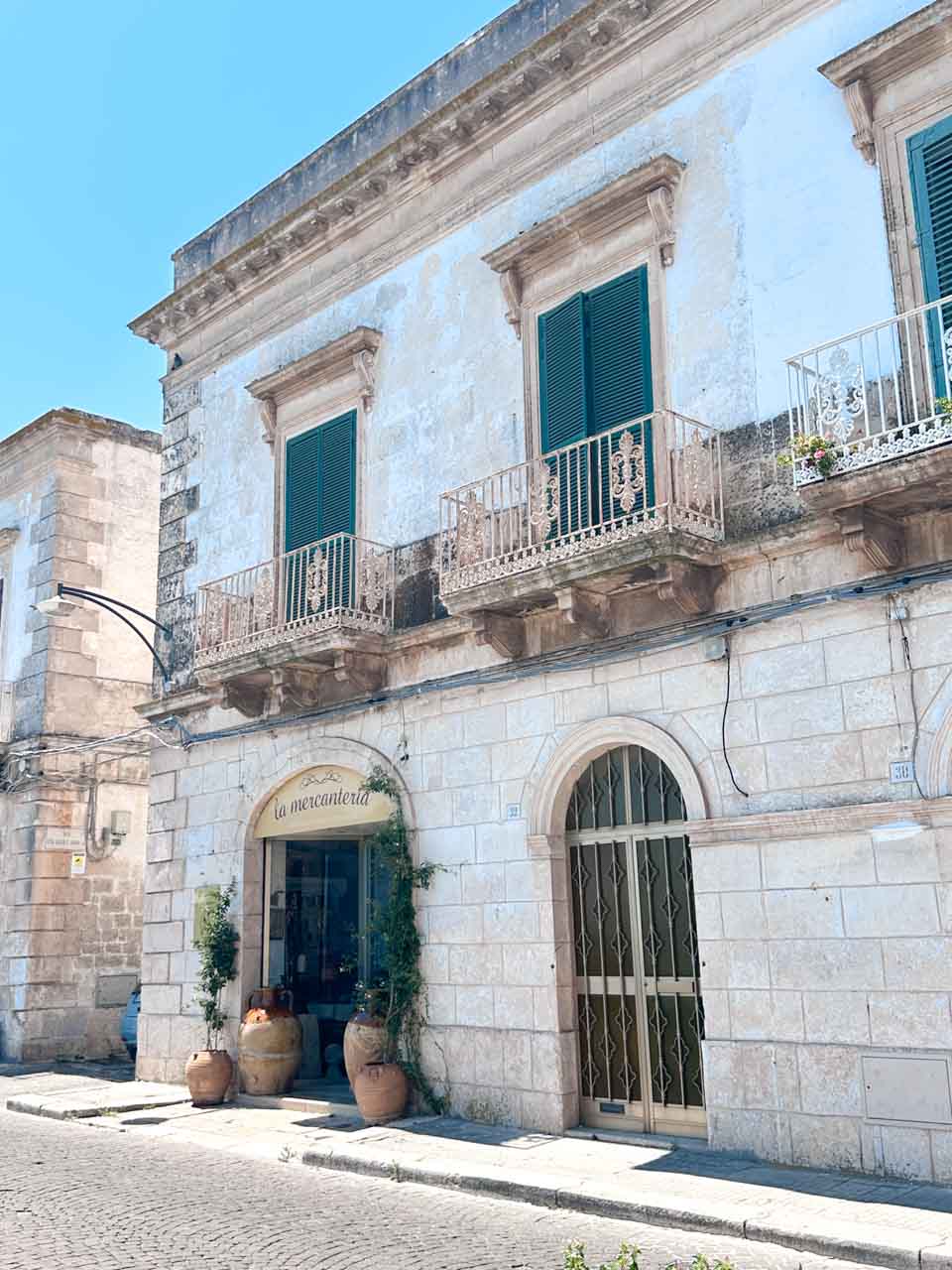 Historic building with green shutters and balconies on a quiet street in Ostuni, Italy