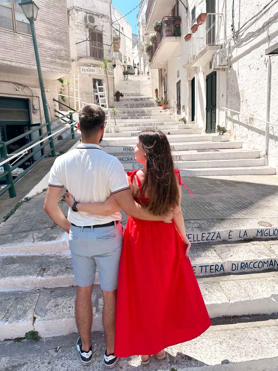 Couple standing on stairs with Italian quotes written on the steps in Ostuni, Italy