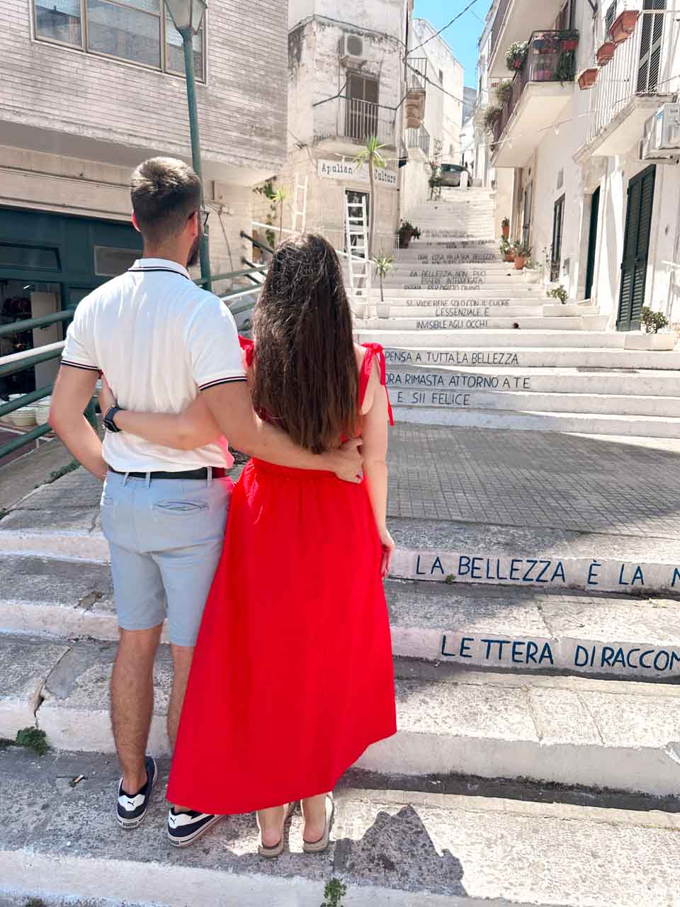 Couple standing on stairs with Italian quotes written on the steps in Ostuni, Italy