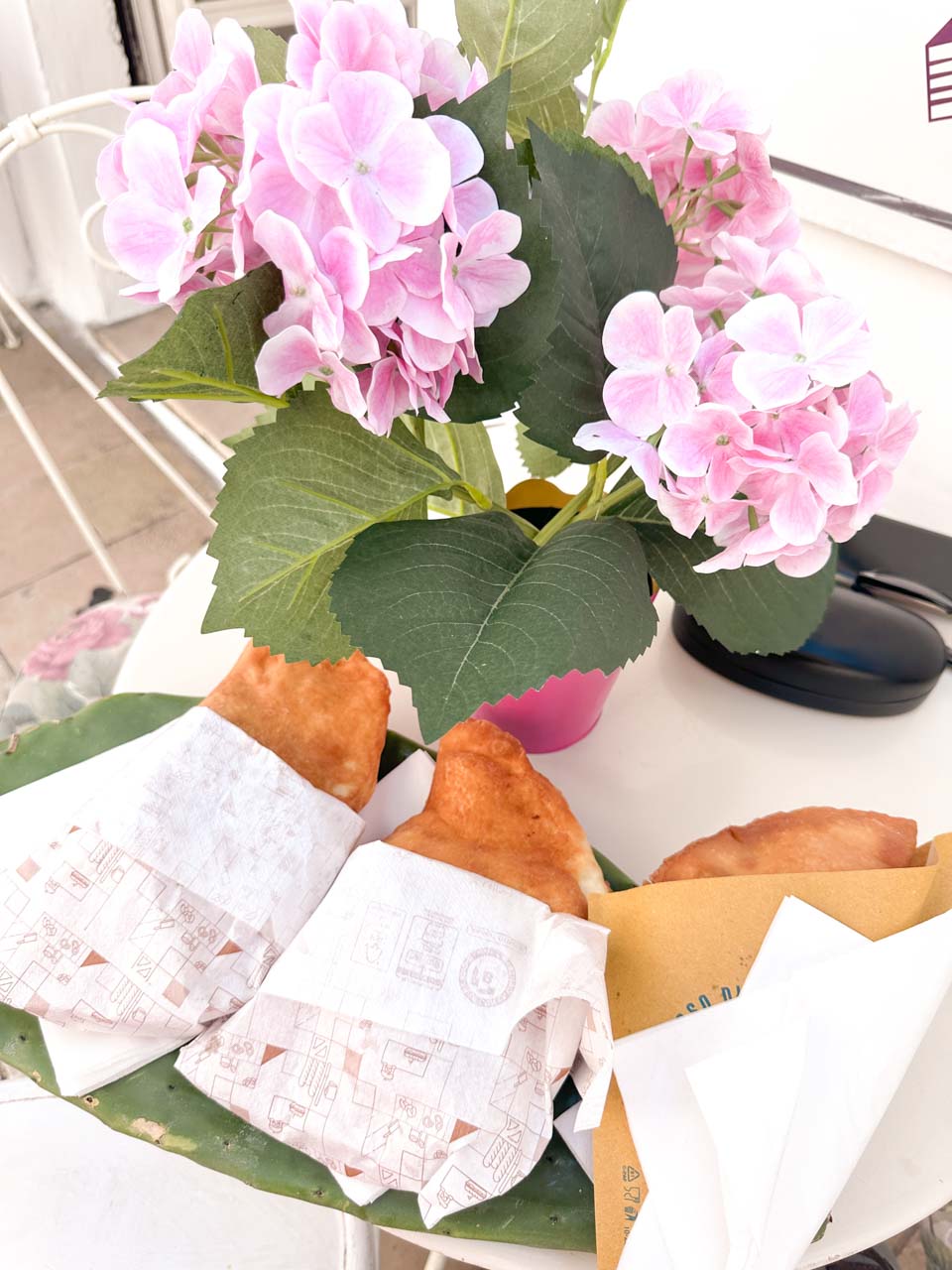 Fried panzerotti wrapped in paper served on a table with pink flowers in Ostuni, Italy