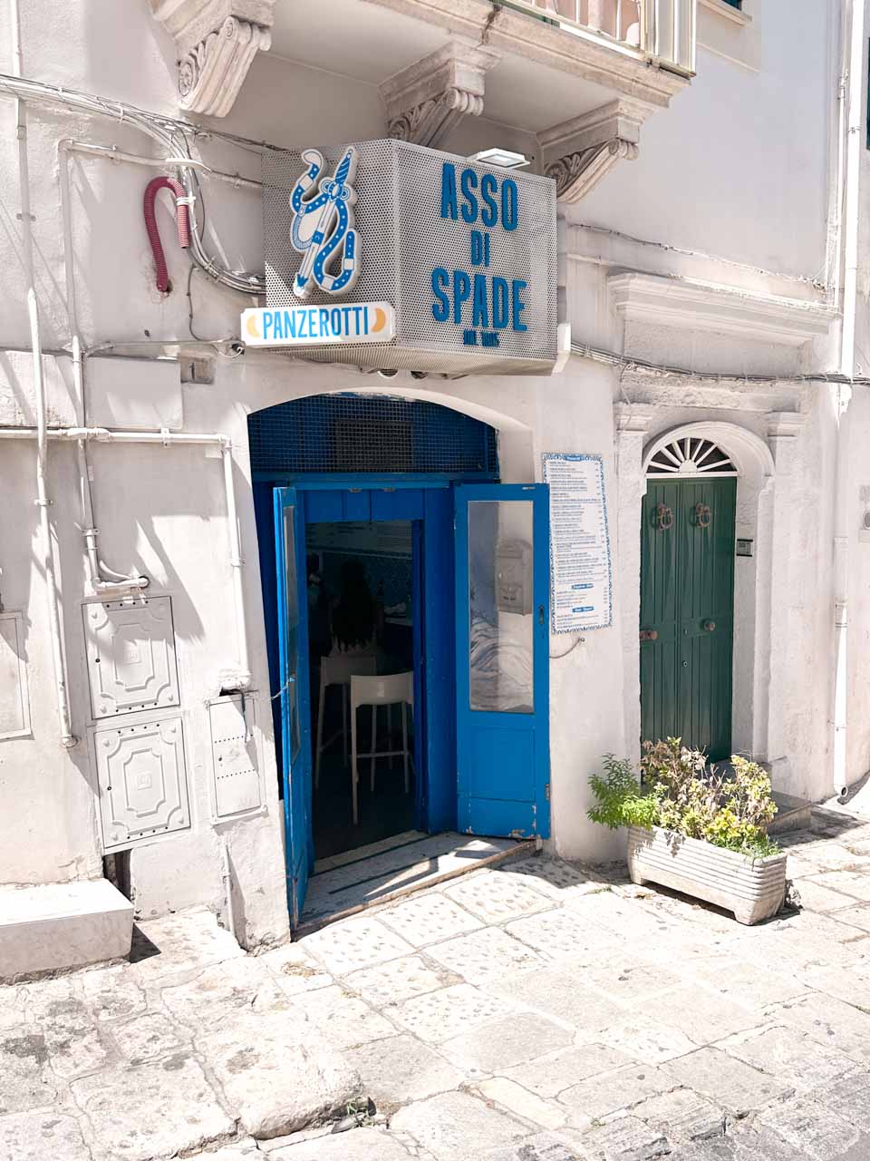 Entrance to Asso di Spade panzerotti shop with a blue door and whitewashed walls in Ostuni, Italy