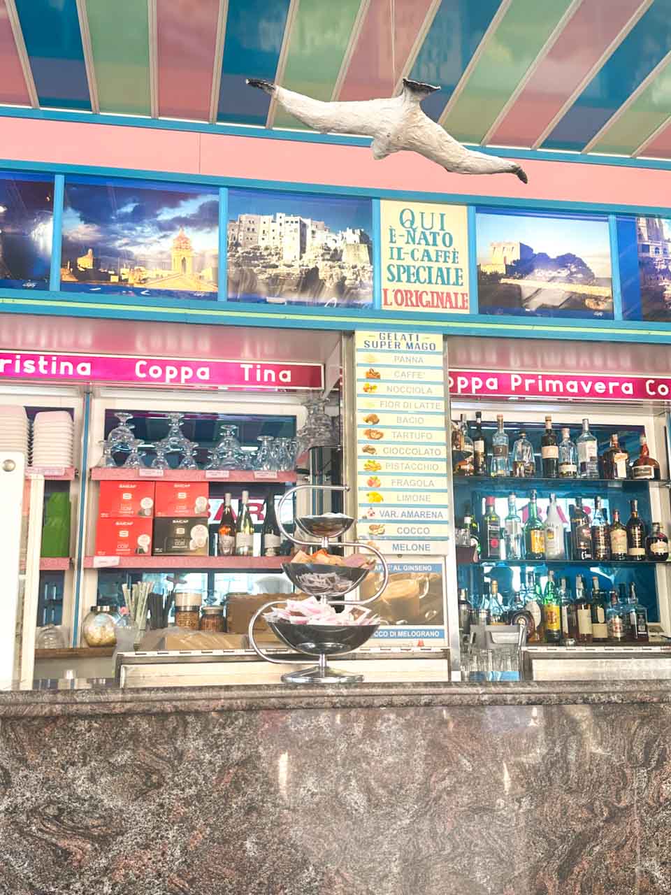 Colourful counter at The Super Mago del Gelo Mario Campanella with a gelato menu, bottles, and a seagull decoration in Polignano a Mare