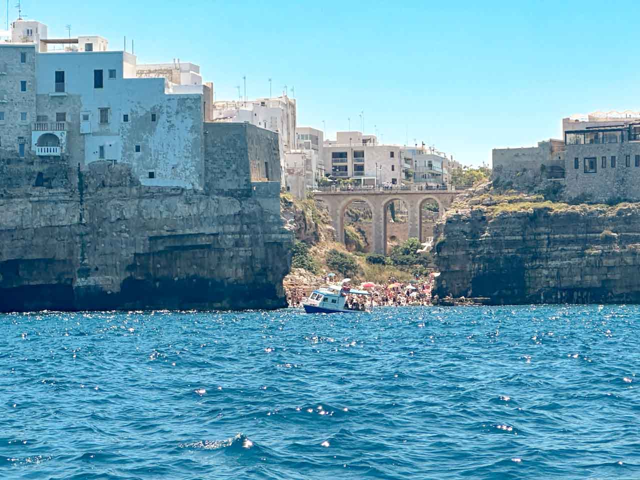 View from the sea of the Lama Monachile (Cala Porto) beach, with a stone bridge and cliffs