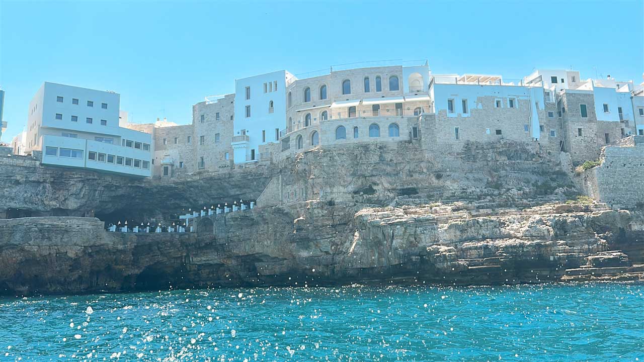 Cliffside buildings above sea caves, with the Grotta Palazzese restaurant built into one of the caves in Polignano a Mare, Italy