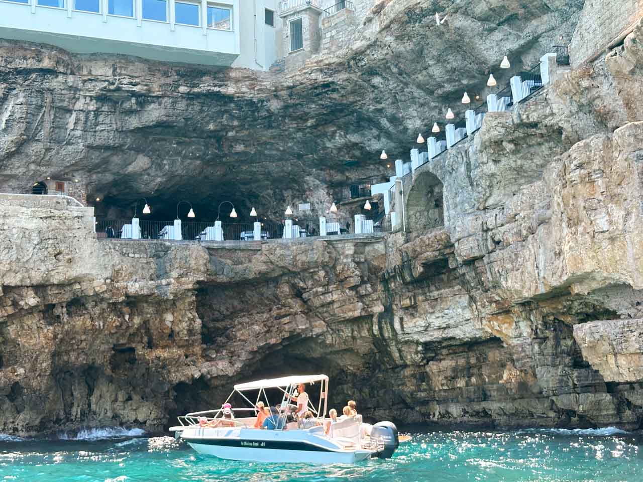 A boat passing the Grotta Palazzese restaurant built into the cliffs above the sea in Polignano a Mare, Italy