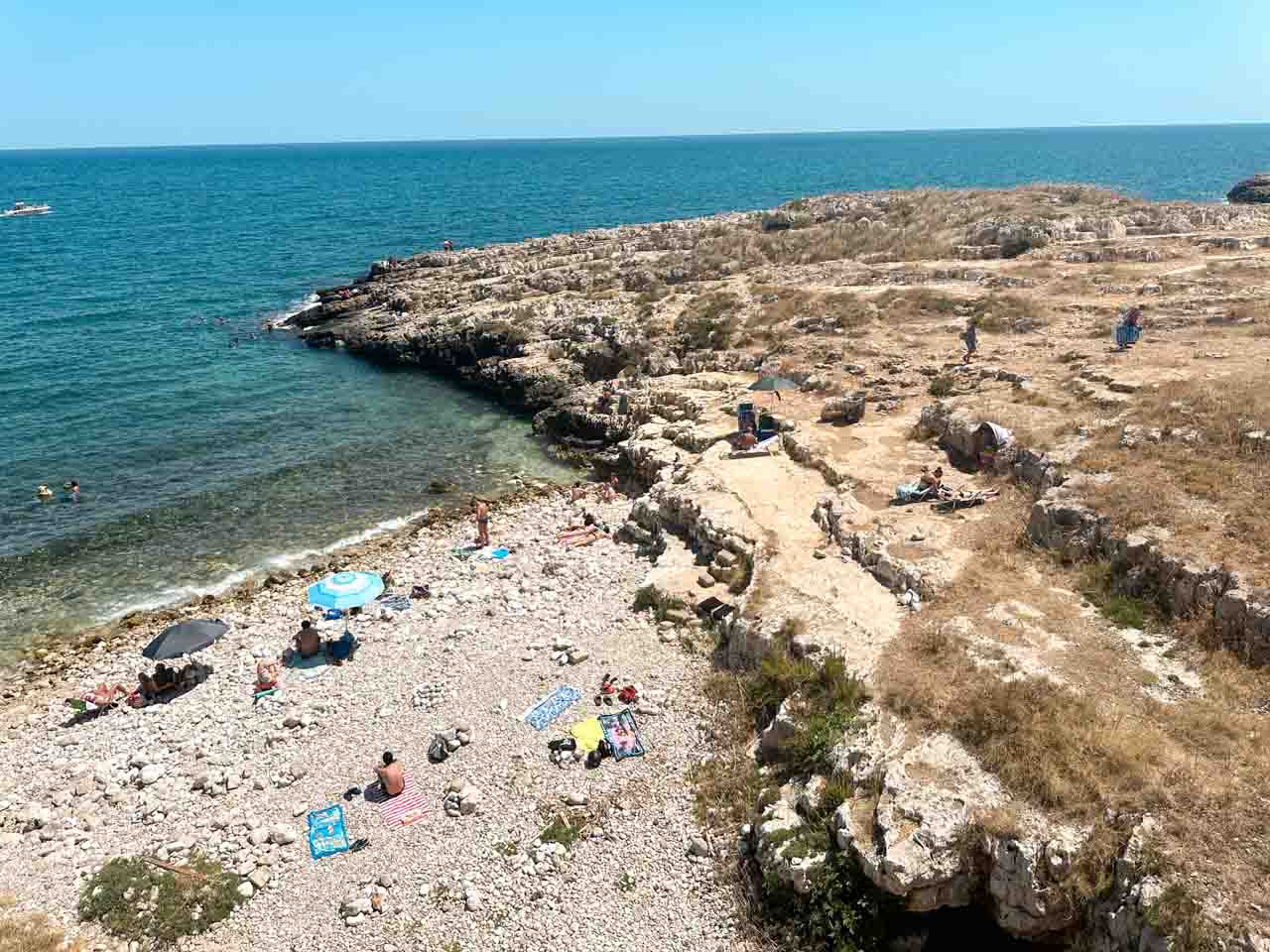A rocky beach with people sunbathing and swimming along the coast in Polignano a Mare, Italy