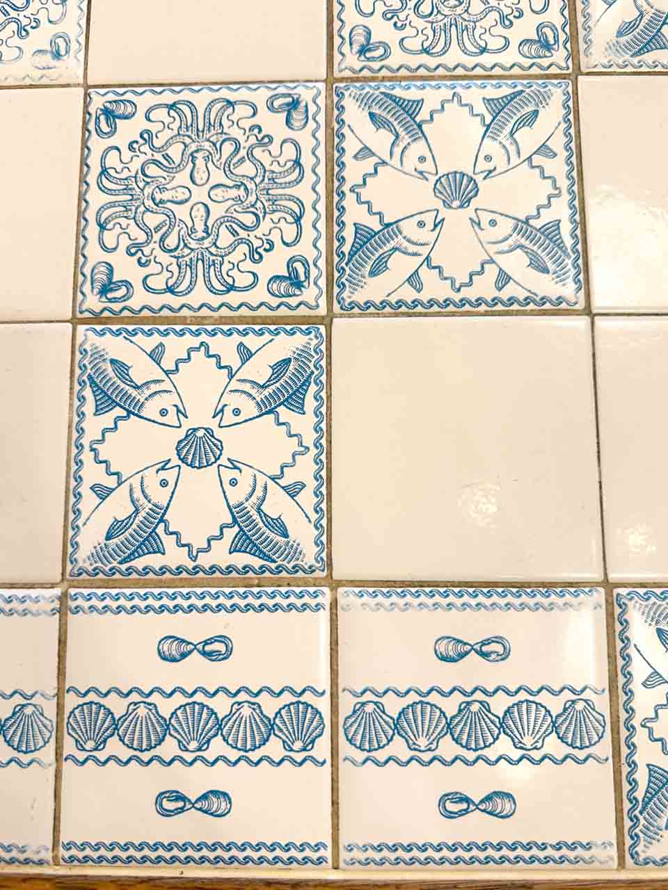Blue and white ceramic tiles with fish and shell patterns on a wall at Pescaria in Polignano a Mare, Italy