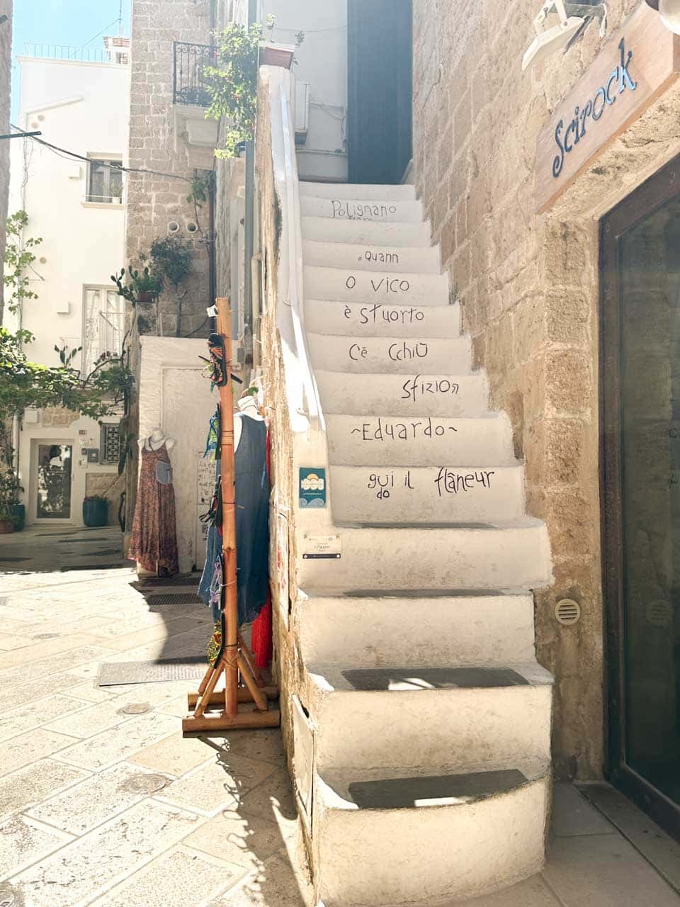 Narrow street in Polignano a Mare with small shops and white steps covered in Italian writing