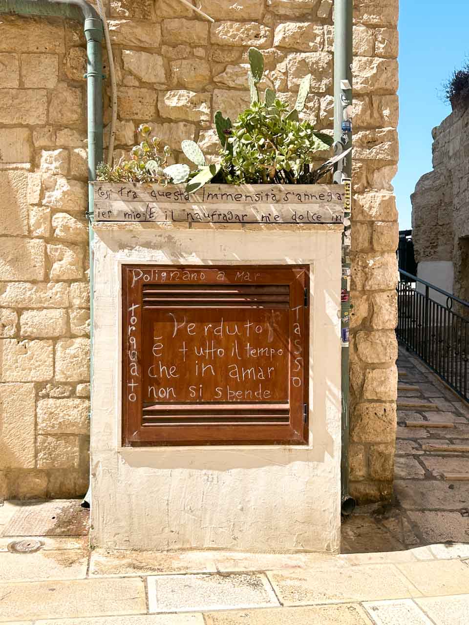 A handwritten Italian quote on a wall with a small cactus planter in Polignano a Mare, Italy