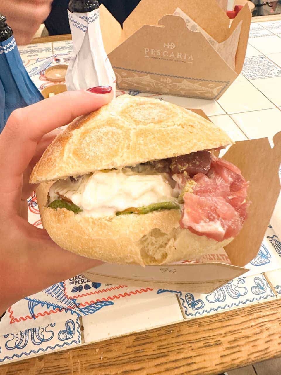 A hand holding a sandwich with tuna tartare, stracciatella cheese, and pesto at Pescaria in Polignano a Mare, Italy