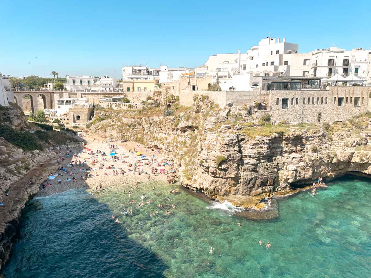 A view from above of the Lama Monachile beach in Polignano a Mare, with swimmers and surrounding cliffs